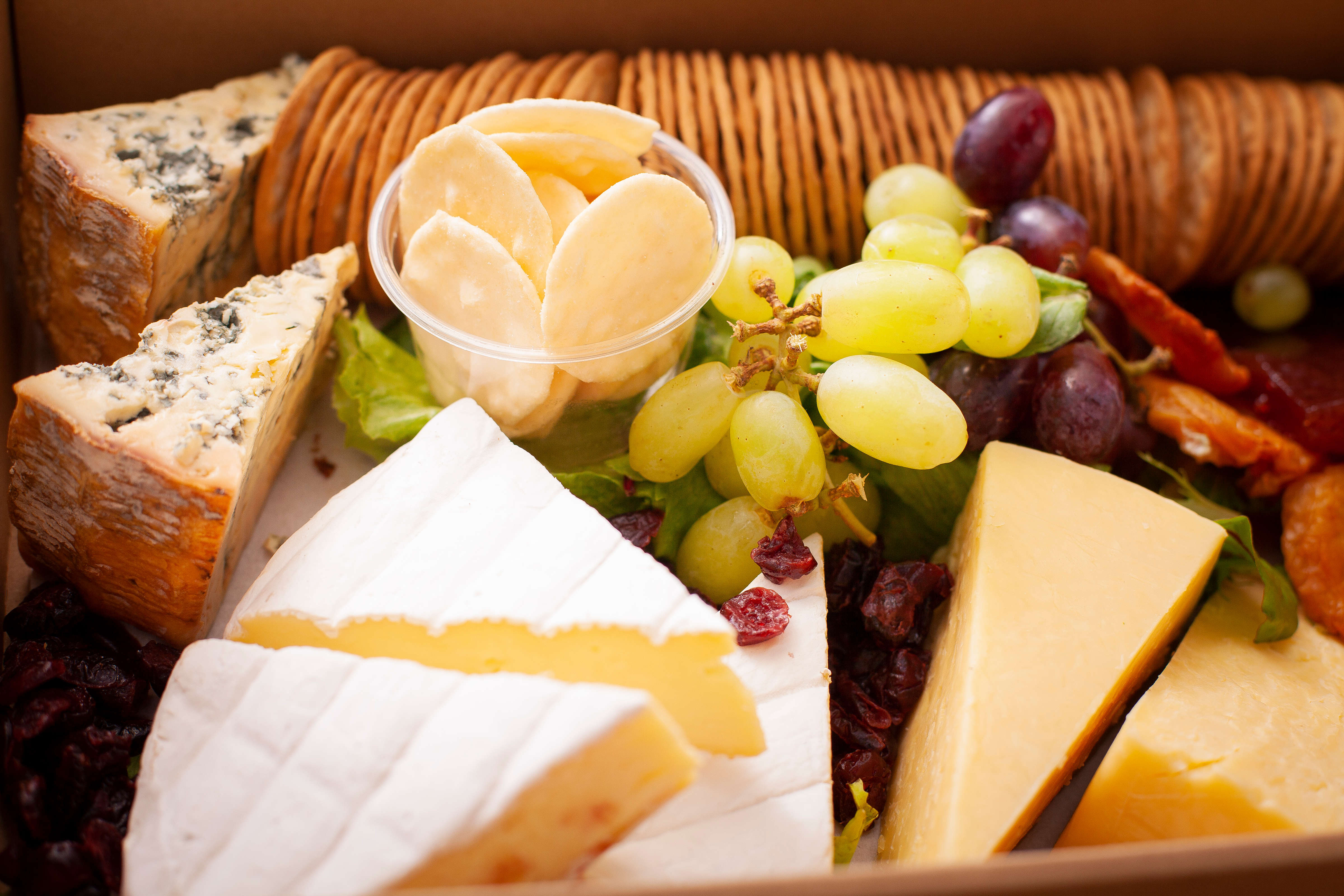 Close up of Tasmanian cheese and cracker box including Brie, Mixed Ashgrove cheddar cheeses, Blue quince paste, dried pears, grapes and crackers. Photo: Richard Jupe.