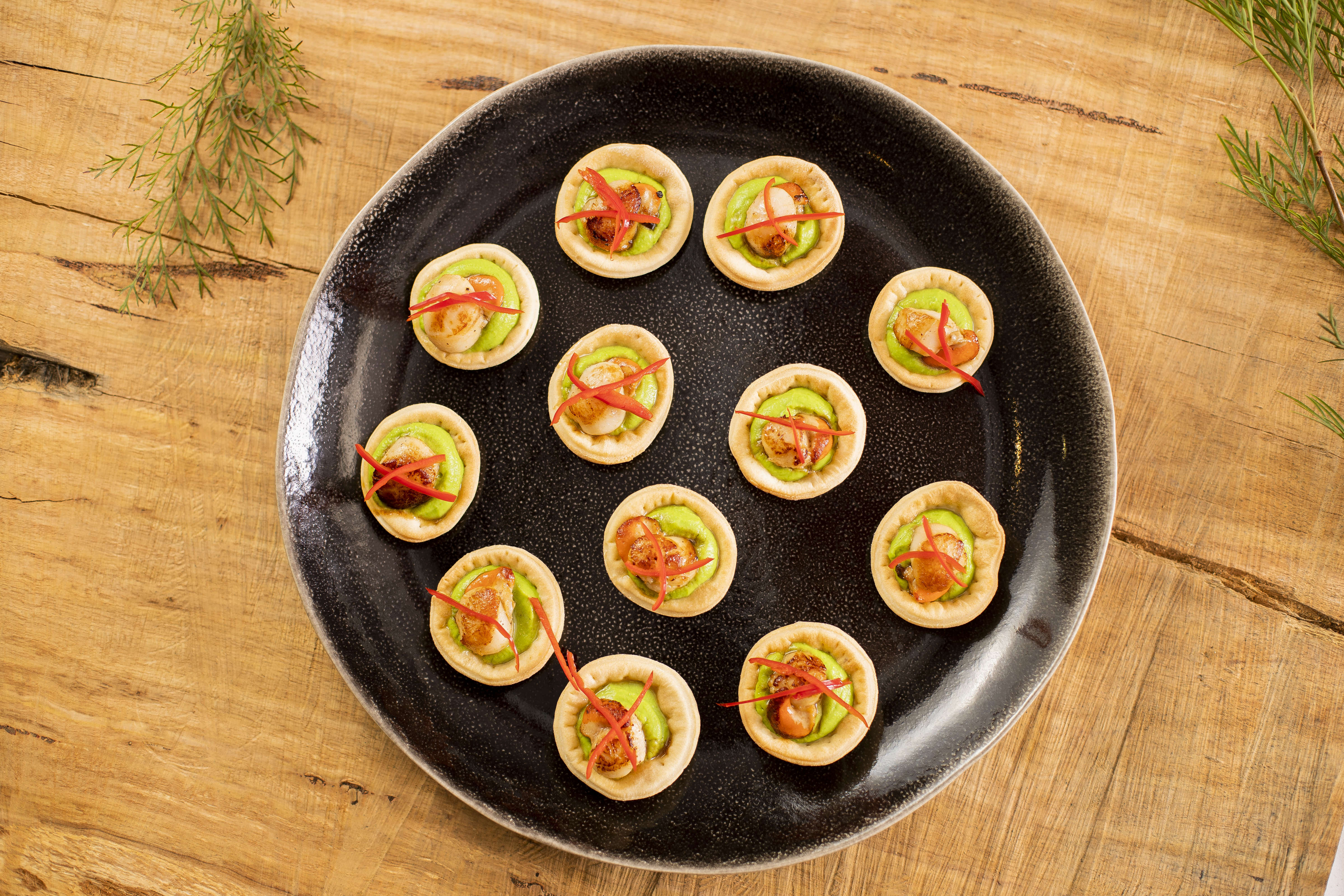 Photo looking down on round platter with tart shells filled with guacamole, panfried scallop, topped with julienne of red capsicum. Photo: Richard Jupe.