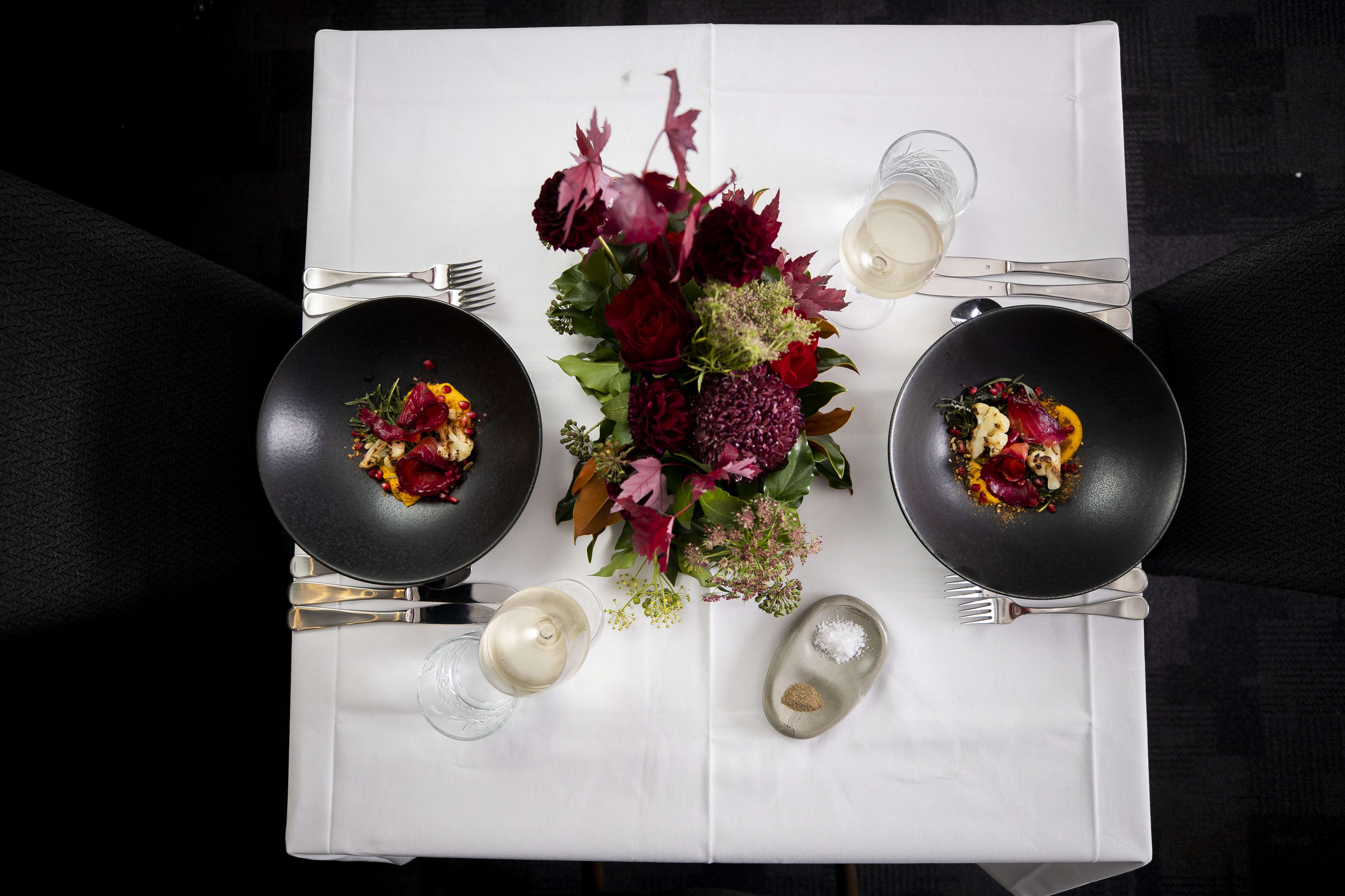 Flat lay photo of a table setting with beetroot cured salmon, cauliflower, carrot puree, pomegranate seeds and dukkaha served in black bowls. Photo: Richard Jupe.