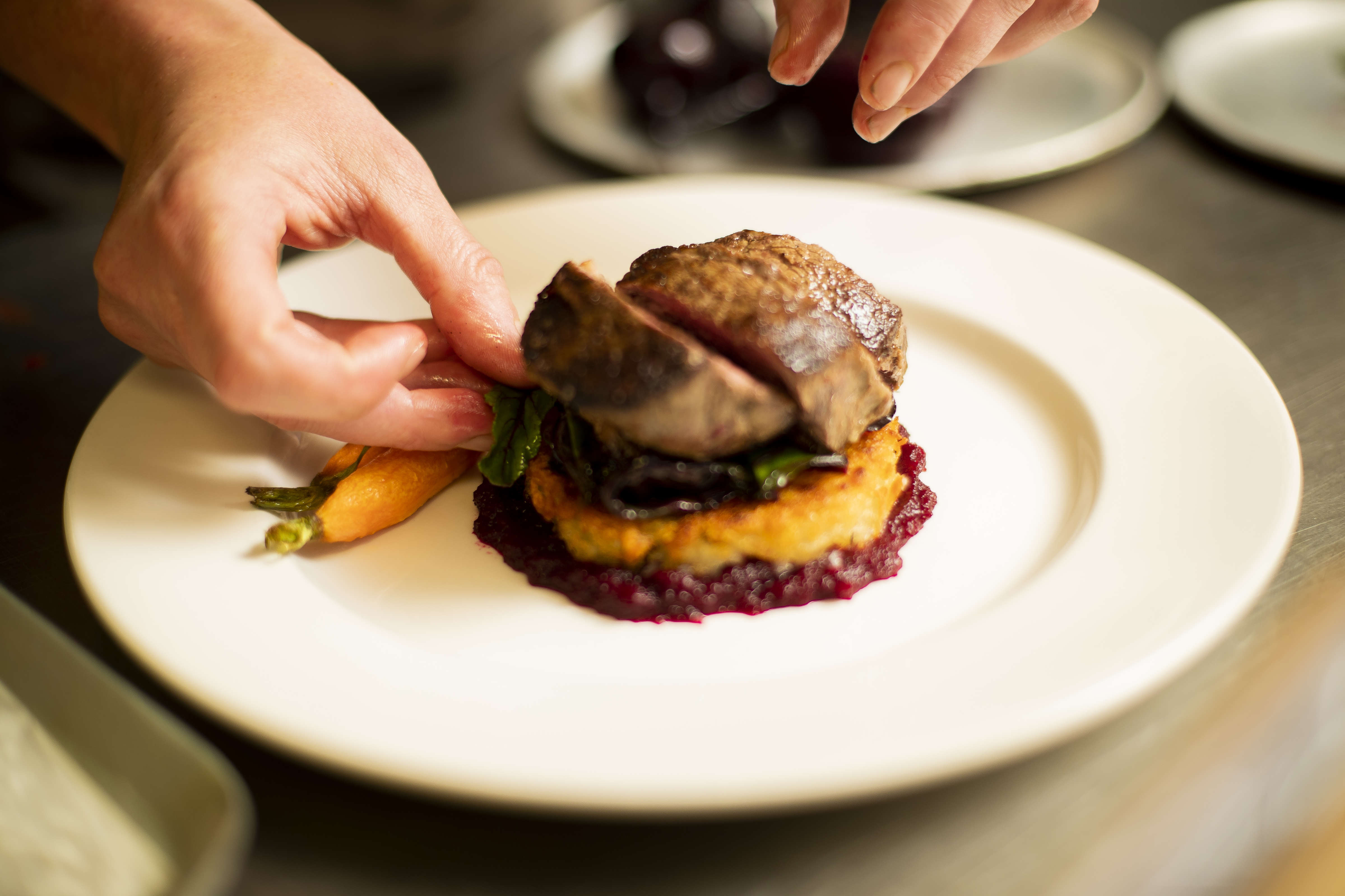 Close up photo of a chef plating up roasted eye fillet slices on hashbrown with beetroot puree and roast baby carrots. Photo: Richard Jupe.