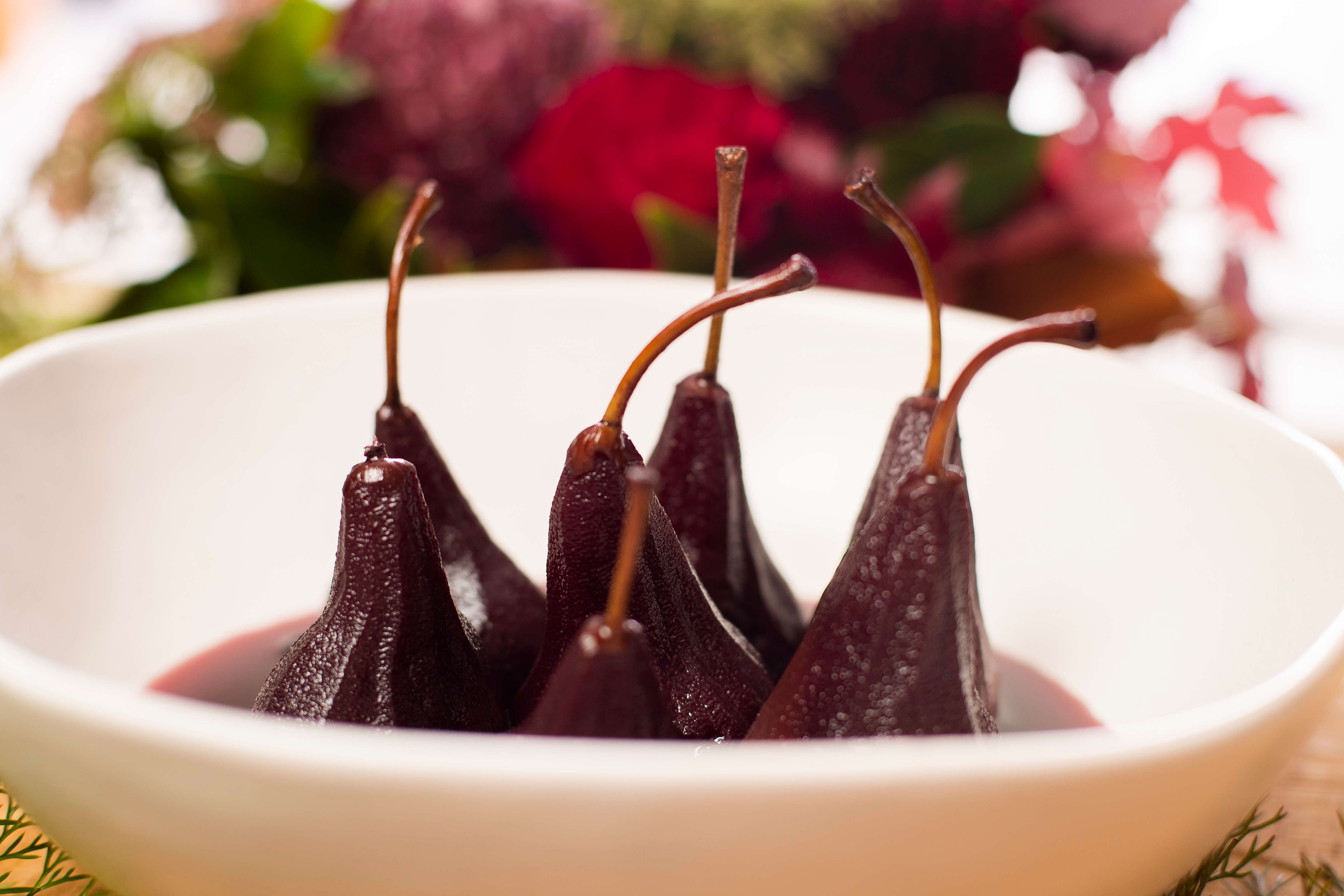 Six pears that have been poached in red wine in a white bowl with syrup. Photo: Richard Jupe.