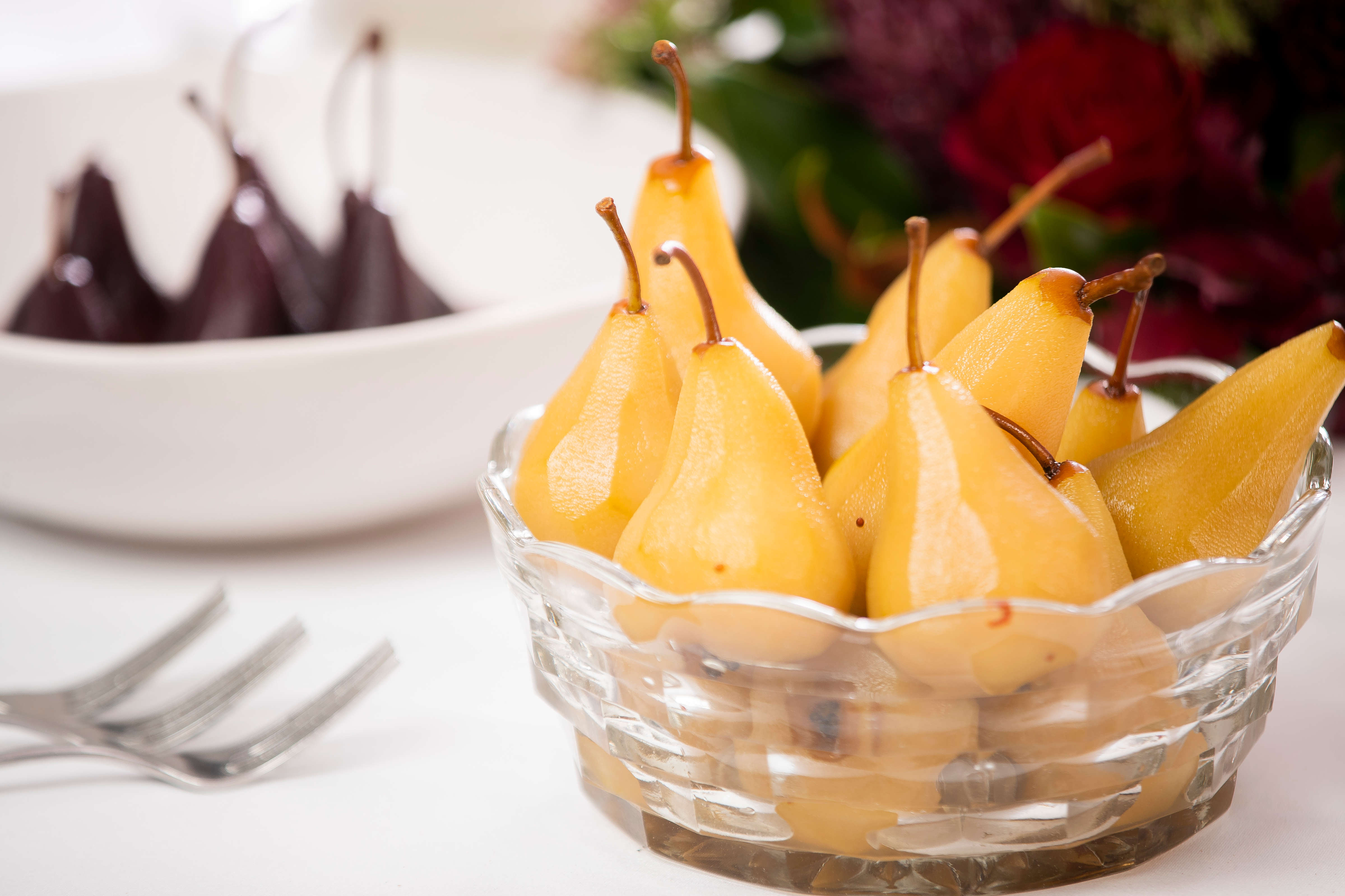 Close up photo of pears that have been poached in saffron syrup in a cut glass bowl with red wine poached pears in the background. Photo: Richard Jupe.