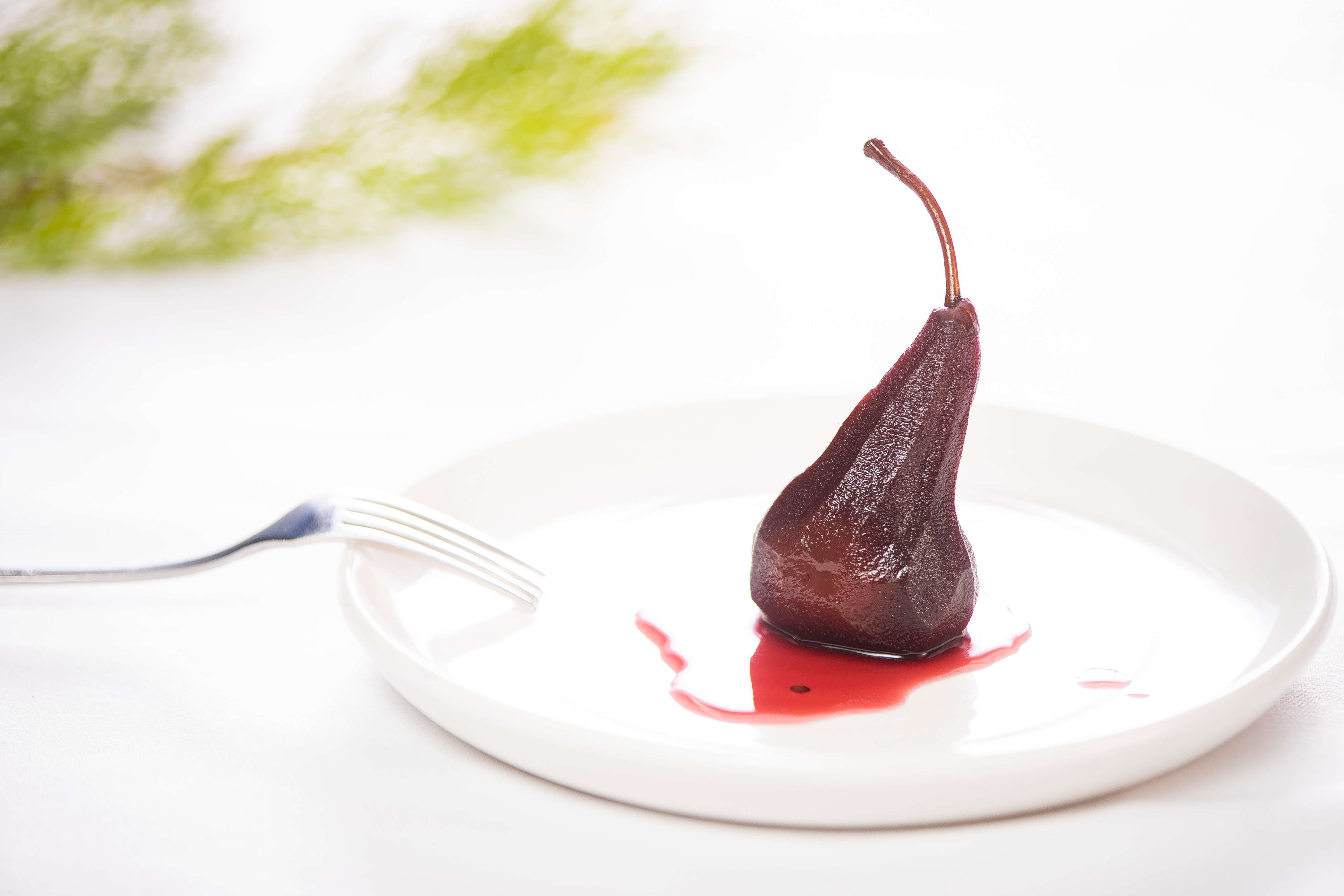 Single red wine poached pear on a white round plate with red wine syrup. Photo: Richard Jupe.