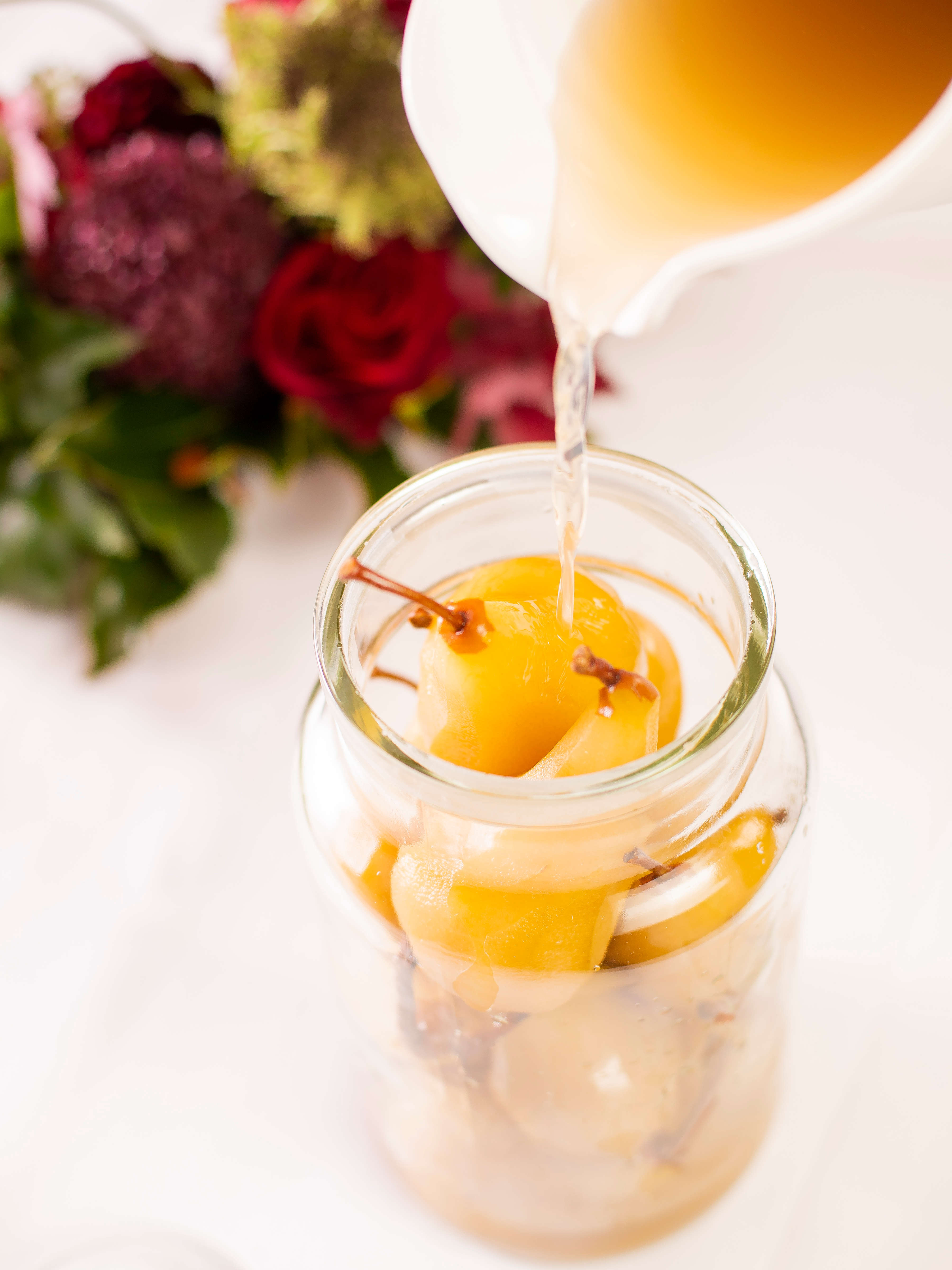 Clear glass jar filled with saffron poached pears with syrup being poured over them. Photo: Richard Jupe.