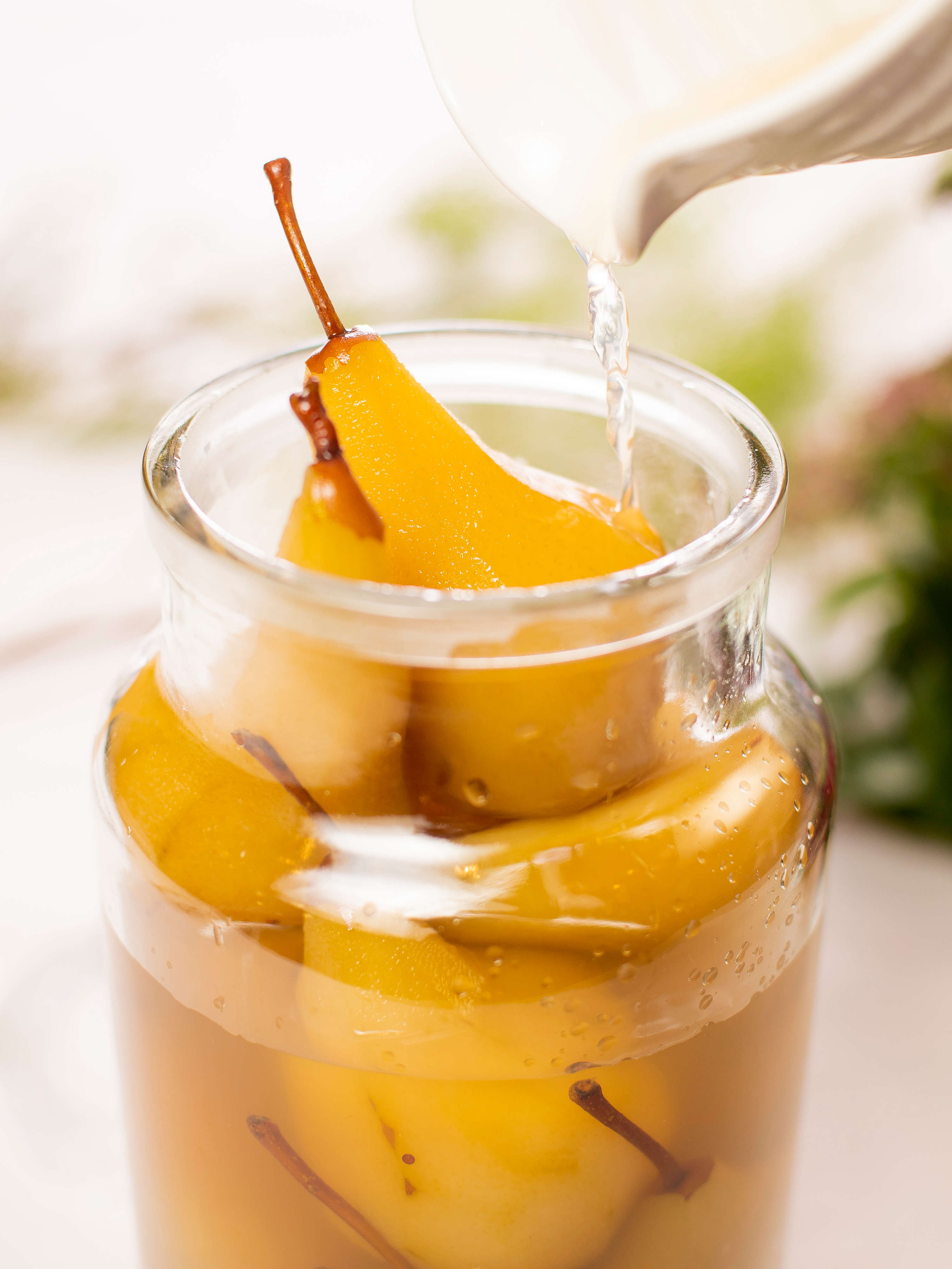 Clear glass jar filled with saffron poached pears with syrup being poured over them. Photo: Richard Jupe.