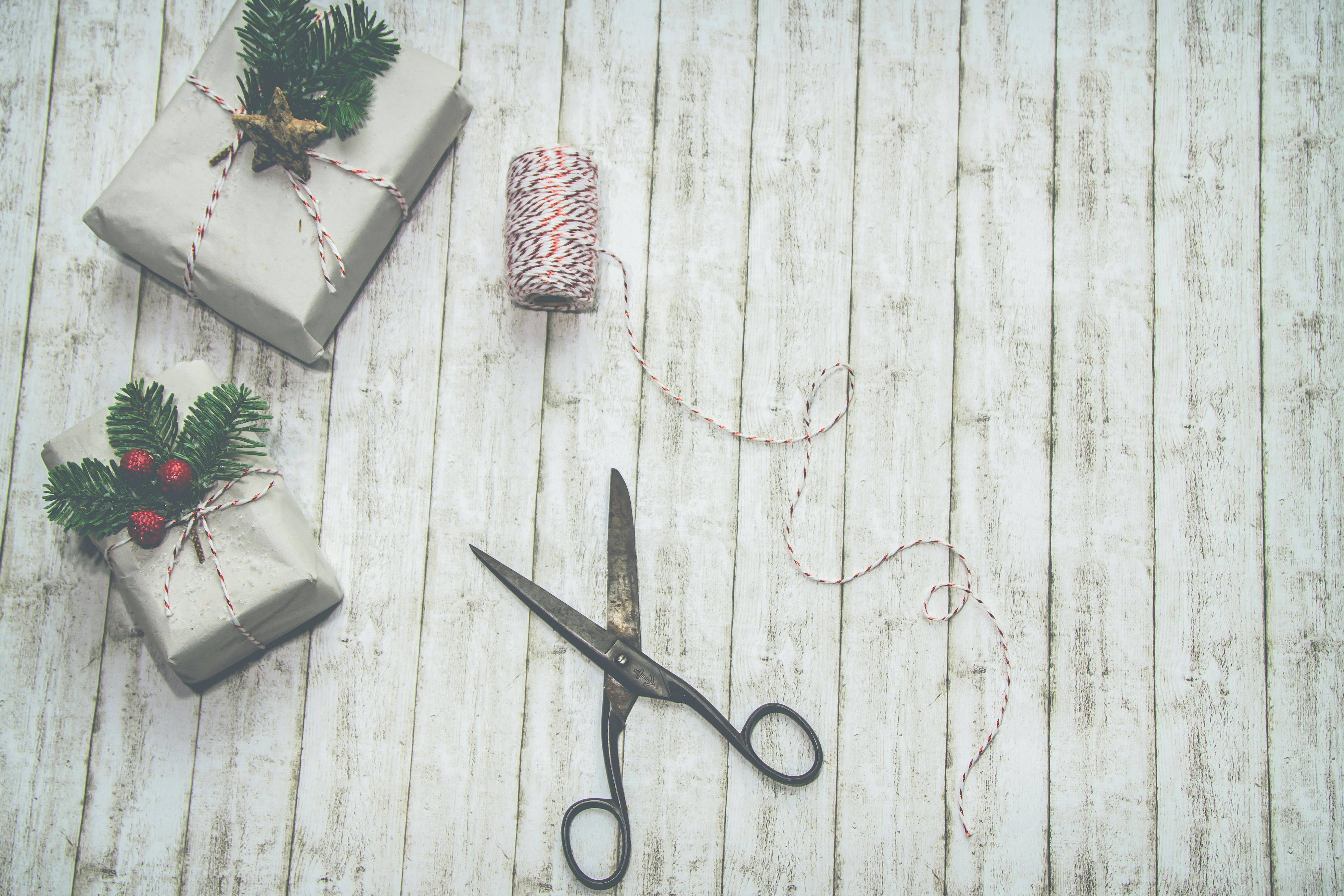 Two Christmas-themed gift boxes wrapped in plain paper, tied with red and white string, and decorated with greenery. Photo: Ylanite Koppens.